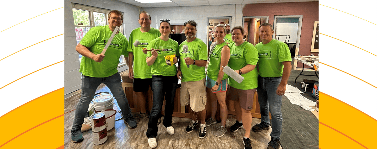 Seven green-shirted painting volunteers from the 2024 Day of Caring smile for the camera