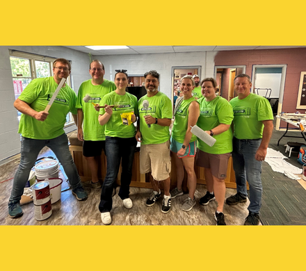 Seven green-shirted painting volunteers from the 2024 Day of Caring smile for the camera
