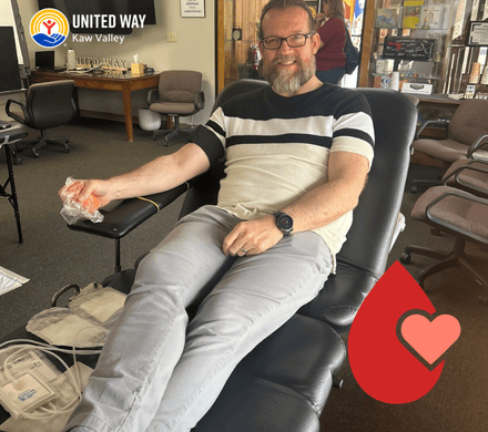 A handsome, smiling human donates blood while relaxing in a comfy lounge chair.