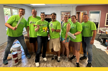 Seven green-shirted painting volunteers from the 2024 Day of Caring smile for the camera