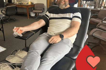 A handsome, smiling human donates blood while relaxing in a comfy lounge chair.